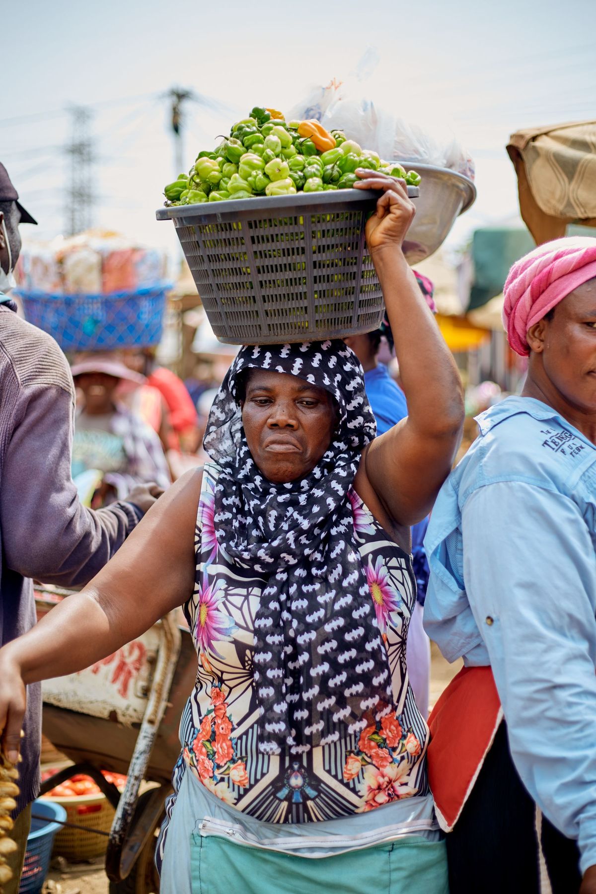A woman at an Accra market carries a basket of green peppers on her head.
